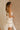 Side view of model sitting while wearing the Rosalind Cream & Black Sheer Tank that has cream sheer fabric, cream lining, black straps, and black tie and ruffle trim details. Worn with matching skirt.