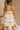 Back view of model sitting while wearing the Rosalind Cream & Black Sheer Tank that has cream sheer fabric, cream lining, black straps, and black tie and ruffle trim details. Worn with matching skirt.