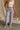Lower body front view of female model wearing the Tatum Periwinkle Denim Pants that have periwinkle denim fabric, a zipper and button fly, cropped raw hem, belt loops, and front and back pockets. Worn with white tank.