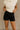 Front view of female model wearing the Ava Washed Black Denim Shorts which features Washed Black Denim Fabric, Two Front Pockets, Two Back Pockets, Silver Button with Zipper Closure and Belt Loops