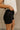 Side view of female model wearing the Ava Washed Black Denim Shorts which features Washed Black Denim Fabric, Two Front Pockets, Two Back Pockets, Silver Button with Zipper Closure and Belt Loops