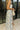 Side view of female model wearing the Felicity White and Blue Floral Maxi Ruffle Dress which features Blue and Green Floral Design, Maxi Length, White Lining, Slit on the side with ruffle details, Square Neckline, Adjustable ruffles straps and Back zipper with hook closure.