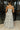 Full body back view of female model wearing the Felicity White and Blue Floral Maxi Ruffle Dress which features Blue and Green Floral Design, Maxi Length, White Lining, Slit on the side with ruffle details, Square Neckline, Adjustable ruffles straps and Back zipper with hook closure.