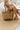 Front view of female model wearing the Beach Please Pearl Woven Tote which features tan rattan woven fabric, "Beach Please" is delicately crafted in pearls on the front and two straps.