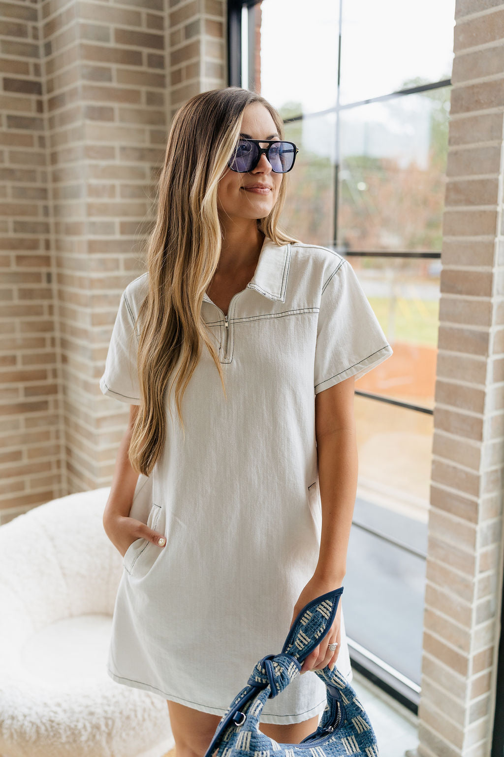 Front view of female model wearing the Chloe White Denim Short Sleeve Mini Dress which features White Denim Fabric, Black Stitch Details, Quarter Zip-Up with Collar Neckline, Front Pockets and Short Sleeves.