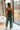 Full body back  view of female model wearing the Jessie Wide Leg Jumpsuit in Green, that features dark green woven material, adjustable straps, and wide legs.Full body front view of female model wearing the Jessie Wide Leg Jumpsuit in Green, that features dark green woven material, adjustable straps, and wide legs. Worn over white bandeau.