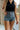 Front view of female model wearing the Nicole Denim Wash Shorts which features Medium Wash Denim, Brown Stitch Details, Two Front Pockets, Two Back Pockets, Belt Loops and scooped hem.