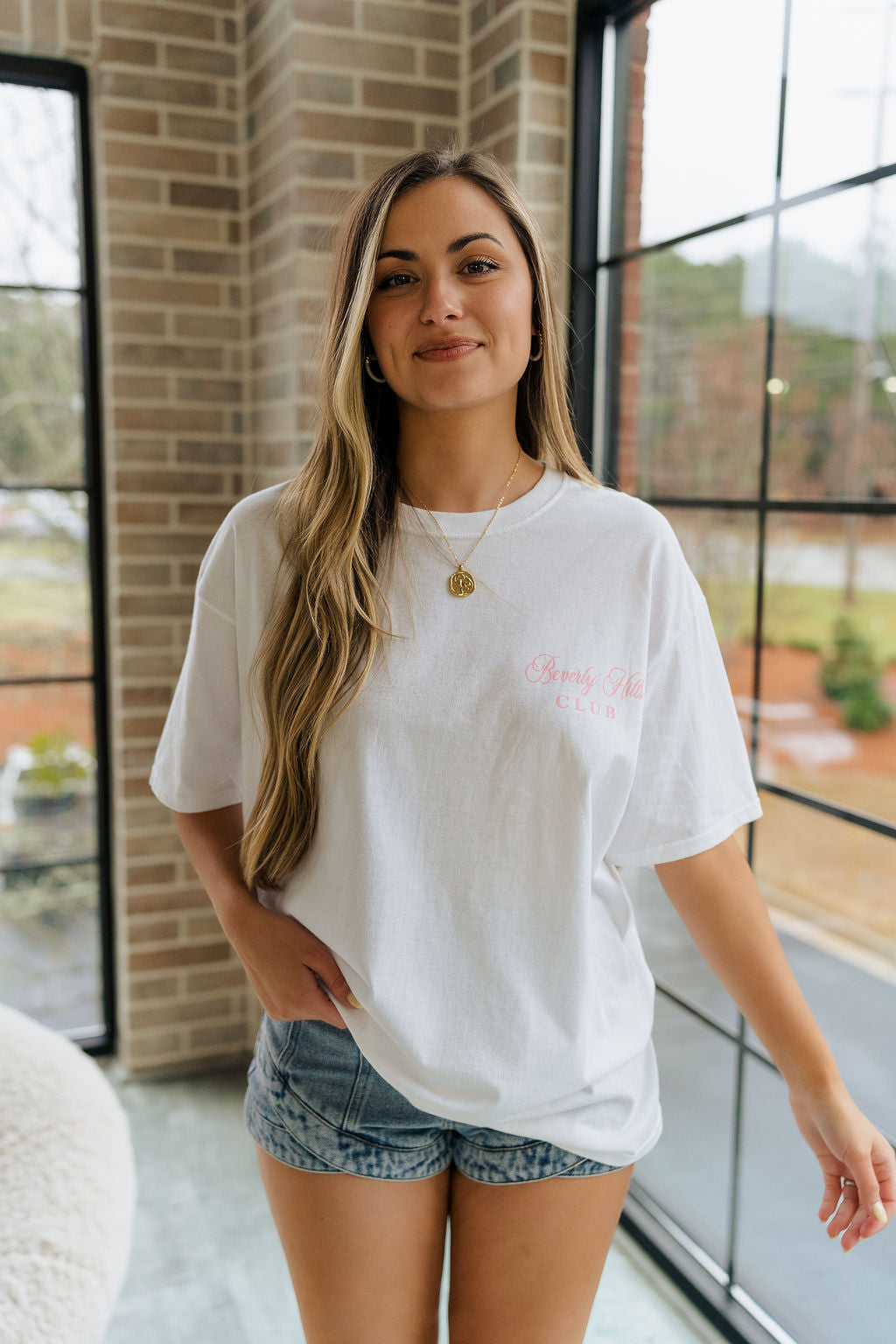 Front view of female model wearing the Beverly Hills Tennis Club Graphic Tee which features White Cotton Fabric, Round Neckline , Short Sleeves, Beverly Hills Tennis Club in pink and green writing.