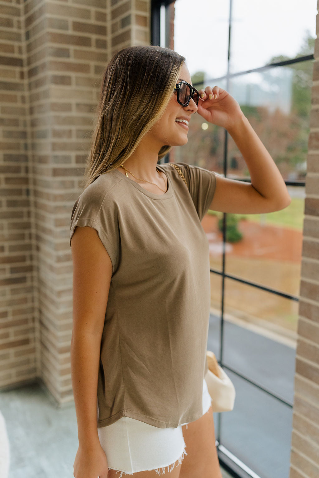 Side view of female model wearing the Amber Light Brown Short Sleeve Top which featuresLight Mocha Brown Lightweight Fabric, Round Neckline and Short Sleeves.