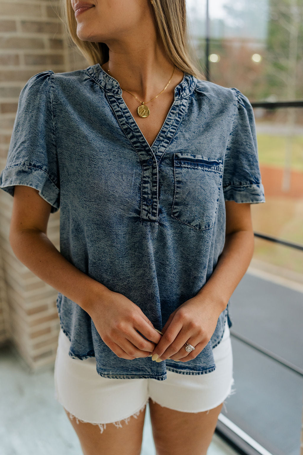 Close up view of female model wearing the Tarah Medium Wash Short Sleeve Top which features washed denim tencel fabric, scooped hem, front left chest pocket, monochrome quarter button up, v-neckline and short sleeves