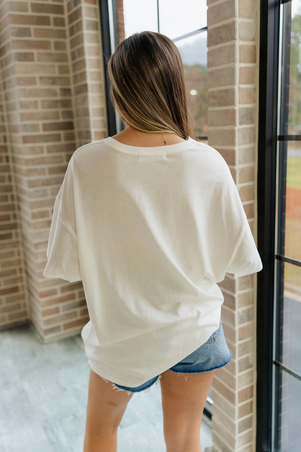 Back view of female model wearing the Melissa Off White Short Sleeve Top which features Off White Cotton Fabric, Round Neckline and Short Sleeves