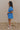 FUll body side view of model wearing the Marissa Blue and White Floral Short Sleeve Romper which features Blue Lightweight Fabric, White Floral Design, Blue Lining, Square Neckline, Short Puff Sleeves and Smocked Back.