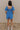 Full body back view of model wearing the Marissa Blue and White Floral Short Sleeve Romper which features Blue Lightweight Fabric, White Floral Design, Blue Lining, Square Neckline, Short Puff Sleeves and Smocked Back.