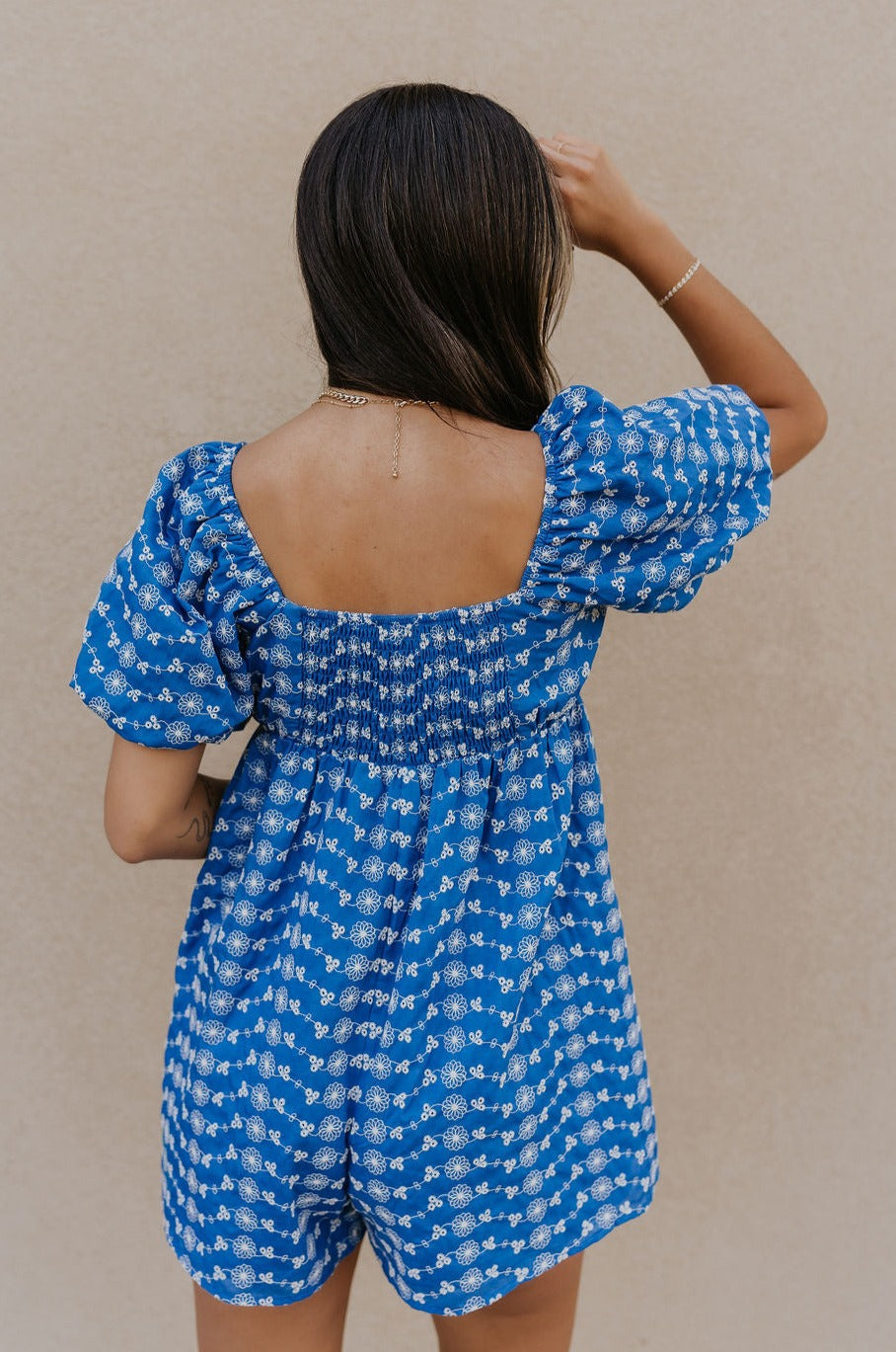 Back view of model wearing the Marissa Blue and White Floral Short Sleeve Romper which features Blue Lightweight Fabric, White Floral Design, Blue Lining, Square Neckline, Short Puff Sleeves and Smocked Back.