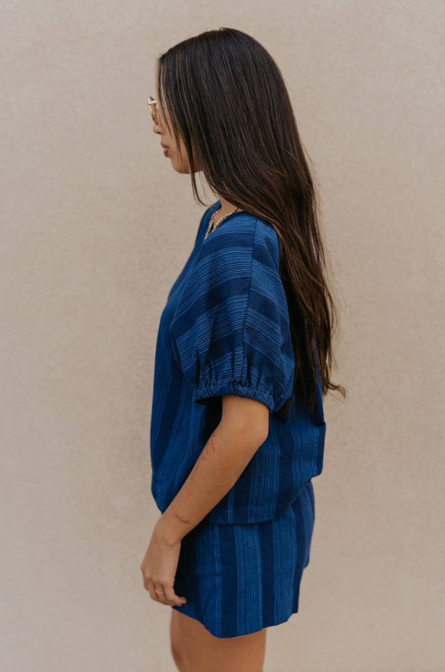 Side view of female model wearing the Julissa Navy Stripe Short Sleeve Top which features Navy Blue with Light Blue Stripe Design, Round Neckline and Short Sleeves