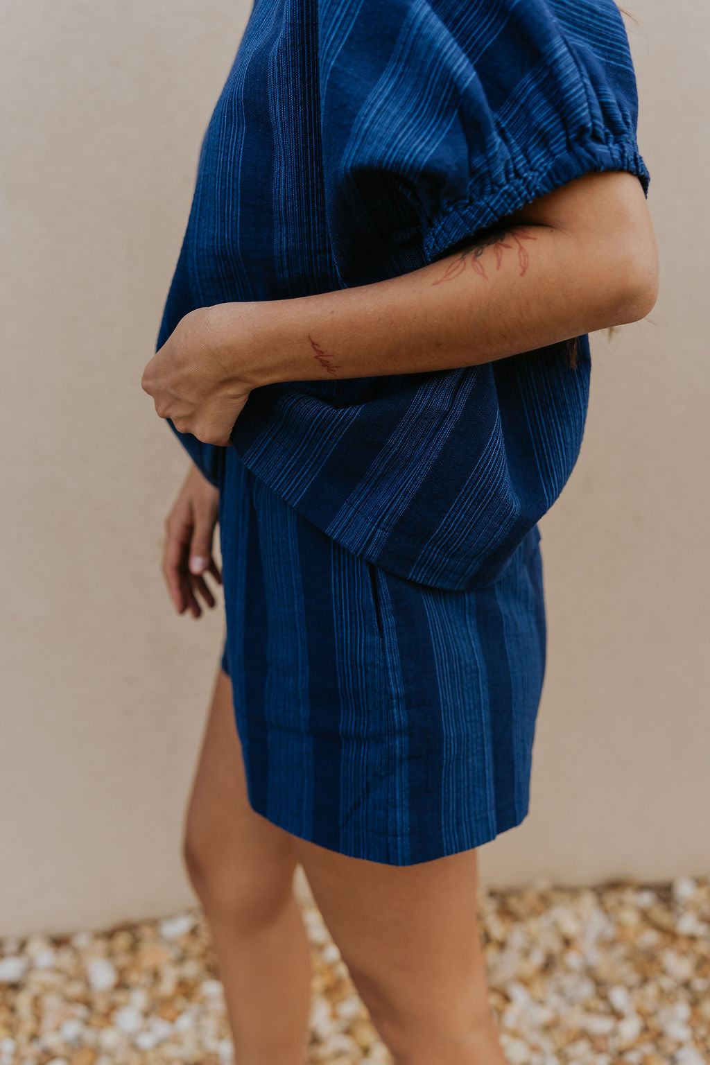 Side  view of female model wearing the Julissa Navy Stripe Shorts which features Navy Blue with Light Blue Stripe Design, Elastic Waistband, Two Front Pockets and Two Back Pockets.