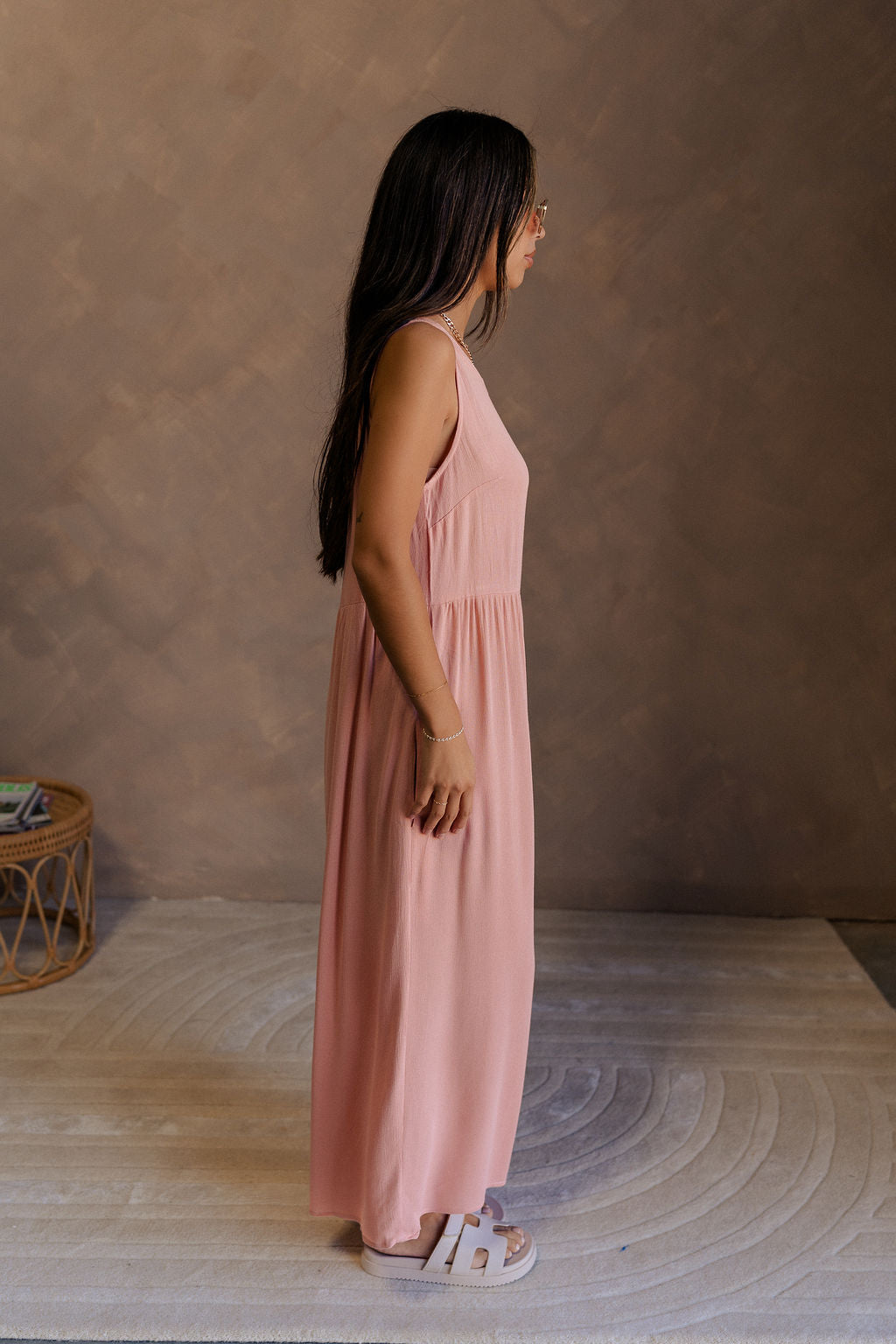 Full body side view of female model wearing the Brooklyn Sleeveless Wide Leg Jumpsuit in salmon pink which features Wide Pant Legs, Two Front Pockets, Lined Pant Legs, Round Neckline and Sleeveless.