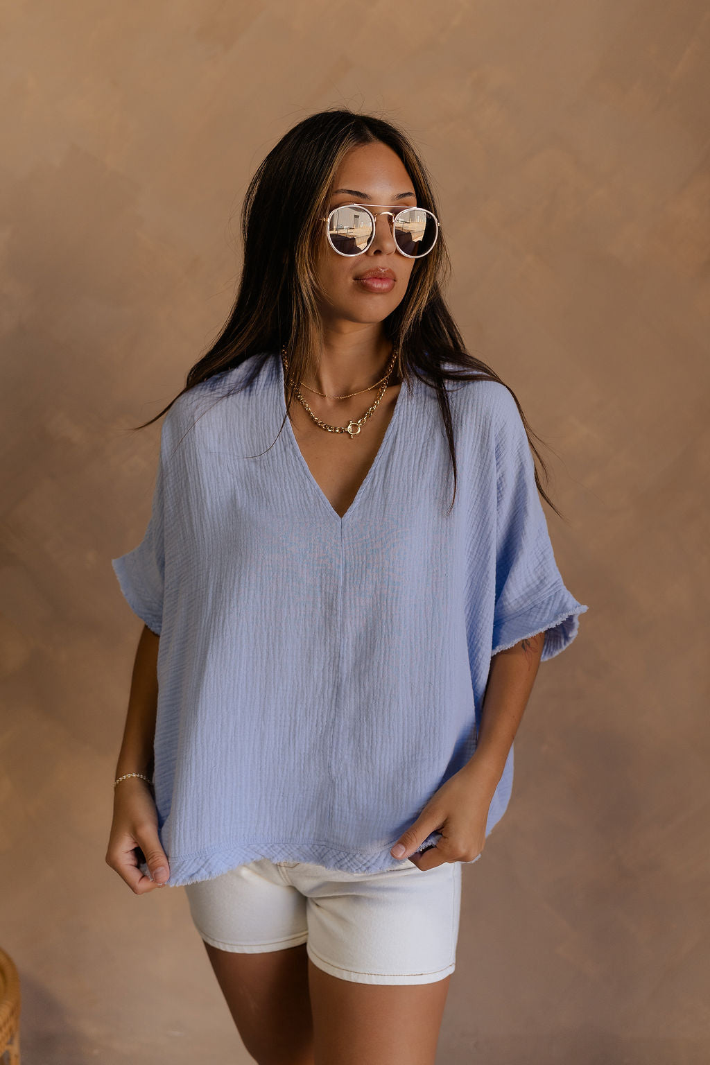 Front view of female model wearing the Nicole Light Blue Gauze Short Sleeve Top which features Light Blue Gauze Fabric, V-Neckline, Short Sleeves and Fray Hem Details.