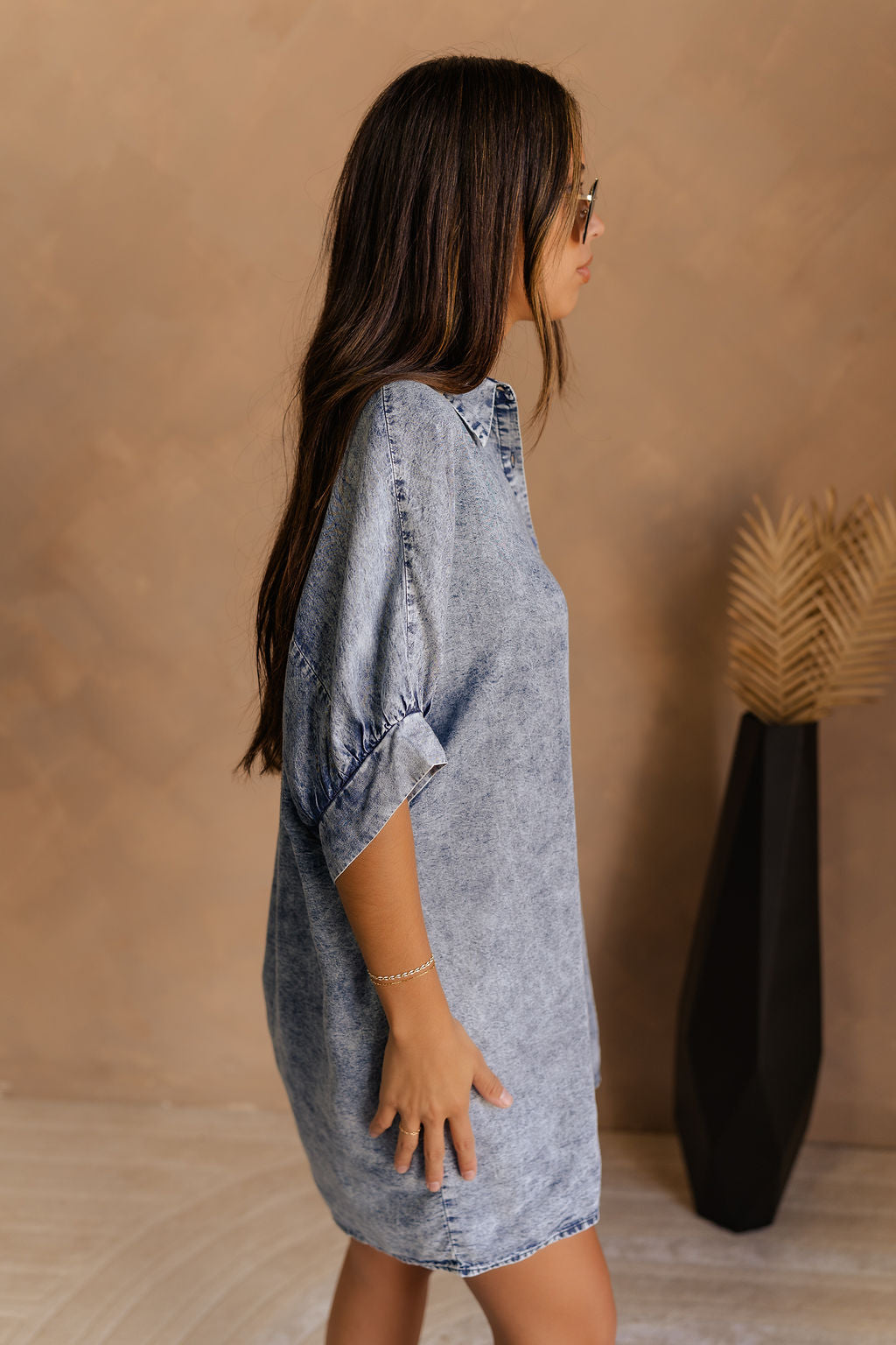 Side view of female model wearing the Emma Button-Up Short Sleeve Mini Dress in Washed Denim which features Tencel Fabric, Mini Length, Front Button-Up Closure, Collared Neckline and Short Puff Sleeves.