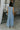 Full body back view of female model wearing the Brooklyn Sleeveless Wide Leg Jumpsuit in light blue which features Wide Pant Legs, Two Front Pockets, Lined Pant Legs, Round Neckline and Sleeveless.
