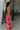 Full body side view of model wearing the Roselyn Pink & Red Floral Maxi Dress that has light pink fabric with dark pink and red floral pattern, a cowl neckline, and spaghetti straps that cross in the back.