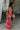 Full body side view of model wearing the Roselyn Pink & Red Floral Maxi Dress that has light pink fabric with dark pink and red floral pattern, a cowl neckline, and spaghetti straps that cross in the back.