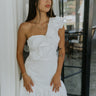 Front view of model wearing the Elyse White Ruffled One Shoulder Dress that has white fabric, one shoulder straps with ruffles, and a ruffled mini length hem.