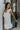 Left side view of model wearing the Elyse White Ruffled One Shoulder Dress that has white fabric, one shoulder straps with ruffles, and a ruffled mini length hem.
