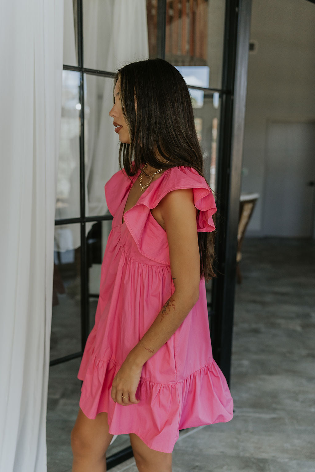 Side view of female model wearing the Alani Pink Ruffle Mini Dress which features Pink Lightweight Fabric, Mini Length, Ruffle Hem, Plunge Neckline and Ruffle Straps