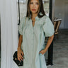 front view of model wearing the Marianna Sage Short Sleeve Dress that has sage green fabric, a button-up front, collar, and short puff sleeves.