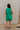 FUll body back view of female model wearing the Serena Zip-Up Sleeveless Romper in Green which features Cotton Fabric, Two Front Pockets, Two Back Pockets, Front Zip-Up Closure, Collared Neckline and Sleeveless.