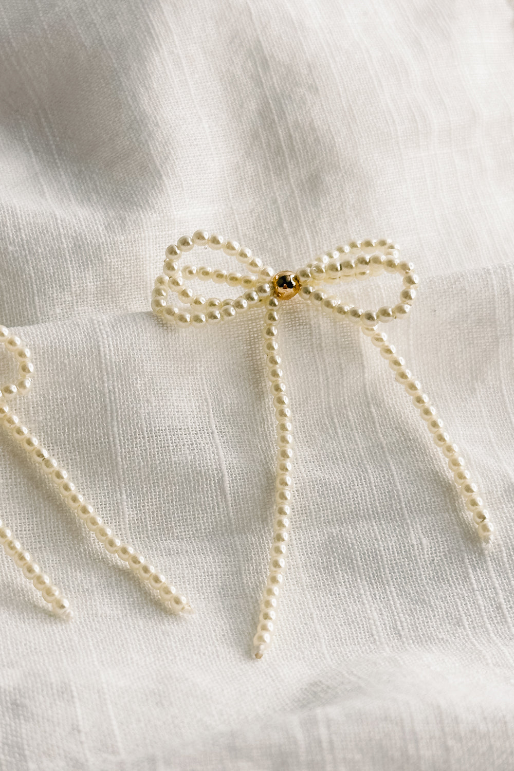 Close up view of the Tarah Cream Pearl Bow Dangle Earrings which features mini cream pearls, single gold pearl detail and shaped as a bow