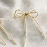 Close up view of the Tarah Cream Pearl Bow Dangle Earrings which features mini cream pearls, single gold pearl detail and shaped as a bow