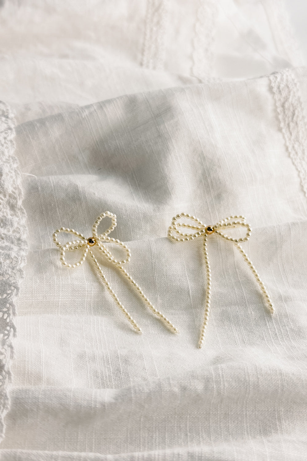 Flat lay view of the Tarah Cream Pearl Bow Dangle Earrings which features mini cream pearls, single gold pearl detail and shaped as a bow