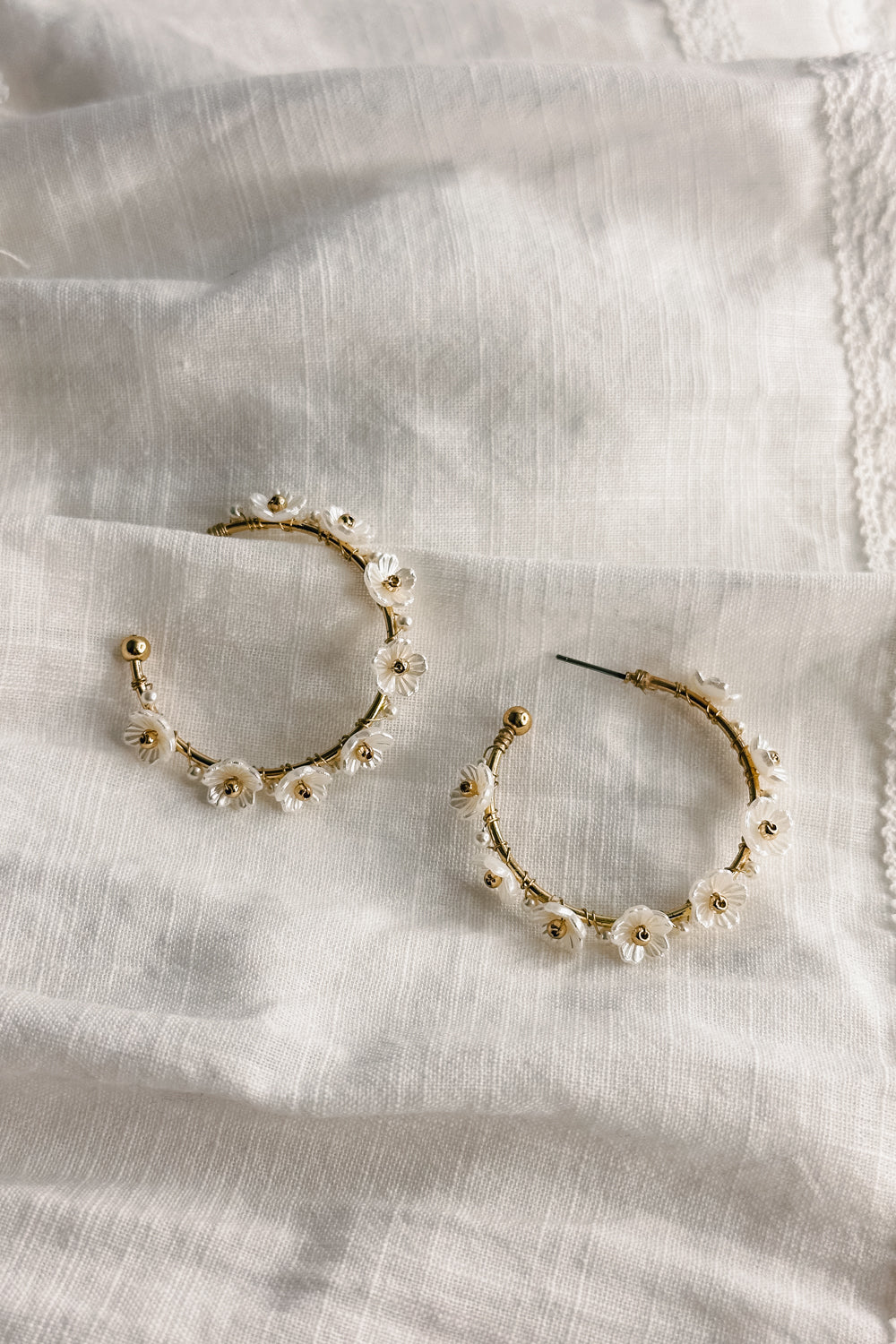 Flat lay view of the Jessie White and Gold Flower Hoop Earring which features medium size open gold hoops, white flower details and back clasp closure