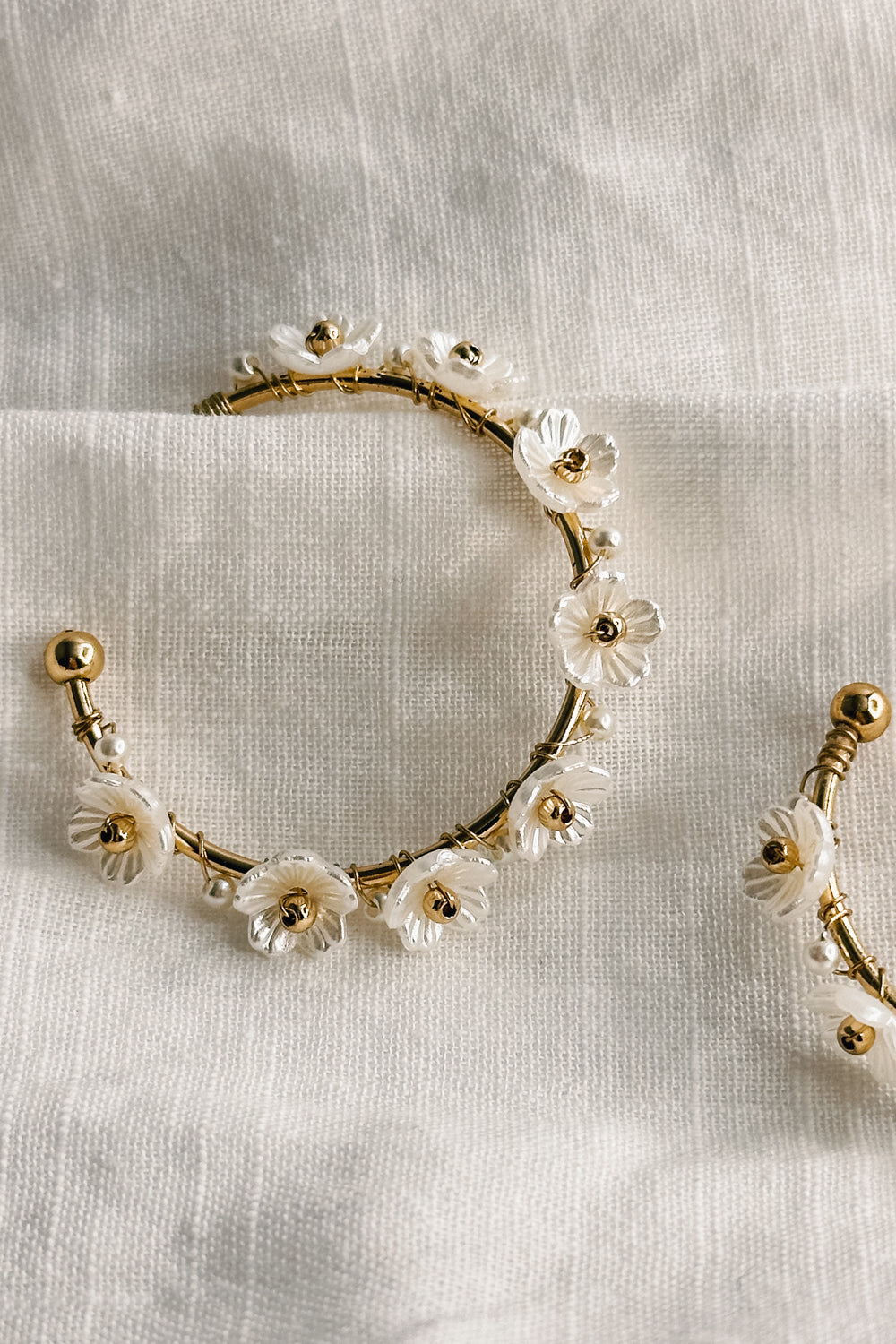 Close up view of the Jessie White and Gold Flower Hoop Earring which features medium size open gold hoops, white flower details and back clasp closure