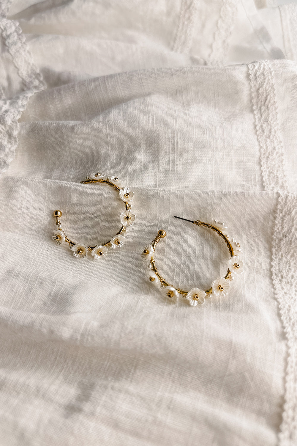 Flat lay view of the Jessie White and Gold Flower Hoop Earring which features medium size open gold hoops, white flower details and back clasp closure
