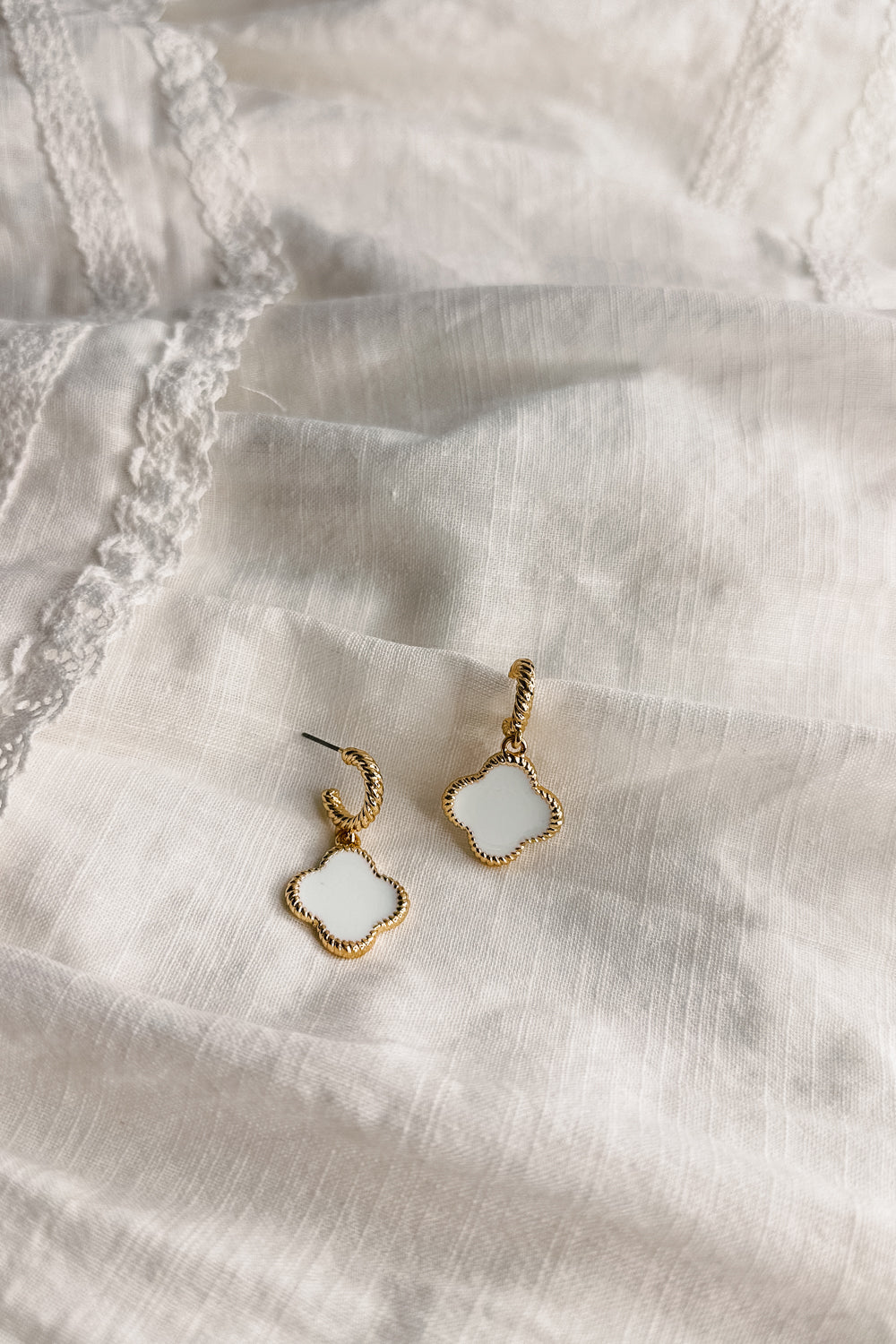Flat lay view of the Fayla White and Gold Clover Earring  which features white clover shaped medallions, gold roped details and ear cuff clasp closure