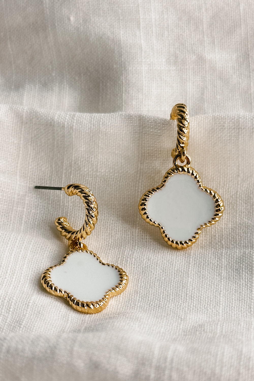 Close up view of the Fayla White and Gold Clover Earring which features white clover shaped medallions, gold roped details and ear cuff clasp closure
