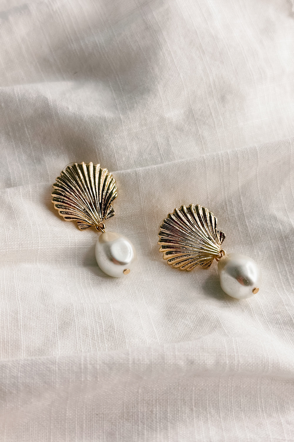 Flat lay view of the Olivia Pearl & Gold Seashell Dangle Earring which features gold seashell shaped studs linked with a pearl medallion