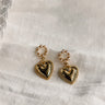 Flat lay view of the Brielle Pearl & Gold Heart Shaped Dangle Earring which features gold heart shaped dangle medallion and pearl details