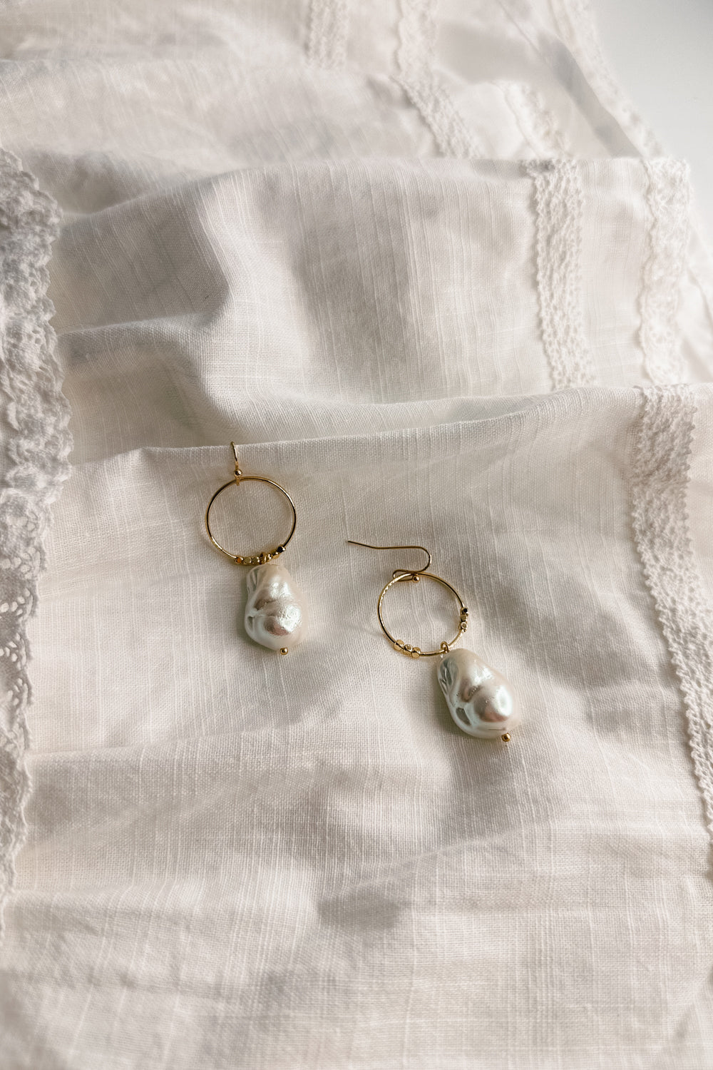Flat lay view of the Shelby Pearl and Gold Mini Hoop Dangle Earring which features small gold hoop with a pearl medallion dangle attached and a hook back closure