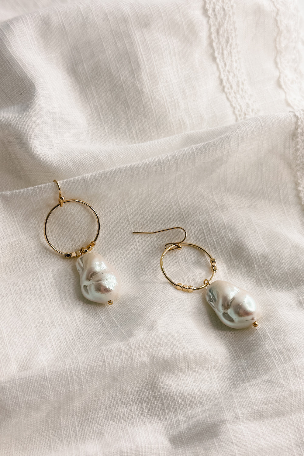 Flat lay view of the Shelby Pearl and Gold Mini Hoop Dangle Earring which features small gold hoop with a pearl medallion dangle attached and a hook back closure