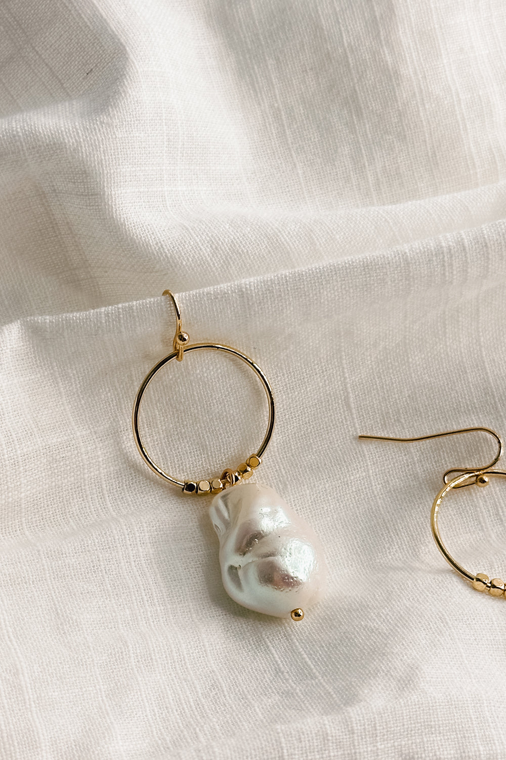 Close up view of the Shelby Pearl and Gold Mini Hoop Dangle Earring which features small gold hoop with a pearl medallion dangle attached and a hook back closure