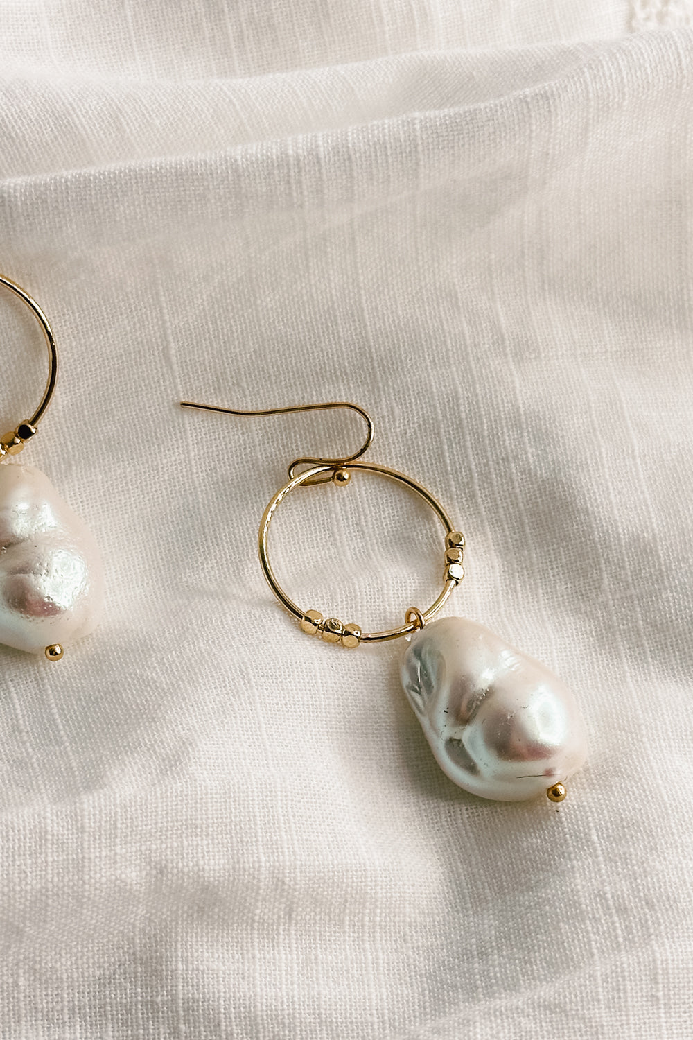Close up view of the Shelby Pearl and Gold Mini Hoop Dangle Earring which features small gold hoop with a pearl medallion dangle attached and a hook back closure
