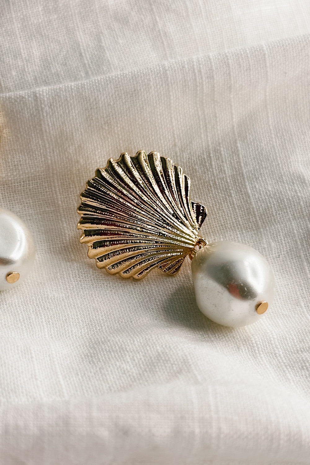 Close up view of the Olivia Pearl & Gold Seashell Dangle Earring which features gold seashell shaped studs linked with a pearl medallion