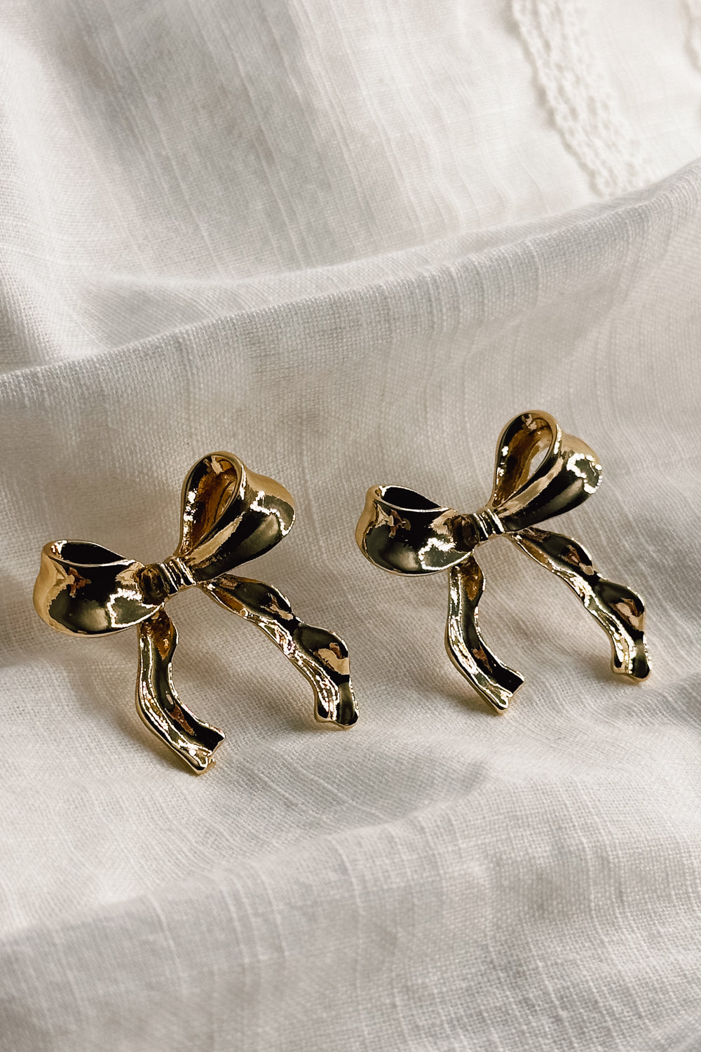 Flat lay view of the Lois Gold Bow Stud Earrings which features gold bow shaped earrings with stud back closures