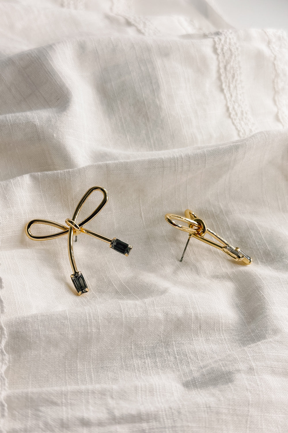 Flat lay view of the Alisa Gold & Baguette Stone Bow Shaped Earring which features gold bow tie shaped earring with baguette clear stone details