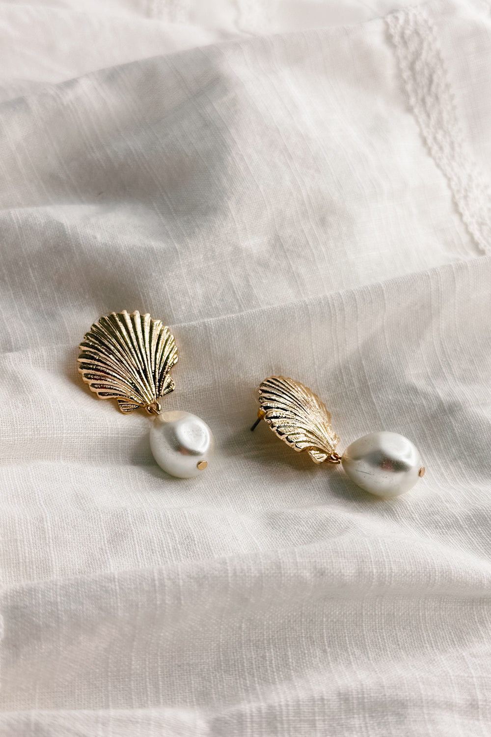 Flat lay view of the Olivia Pearl & Gold Seashell Dangle Earring which features gold seashell shaped studs linked with a pearl medallion
