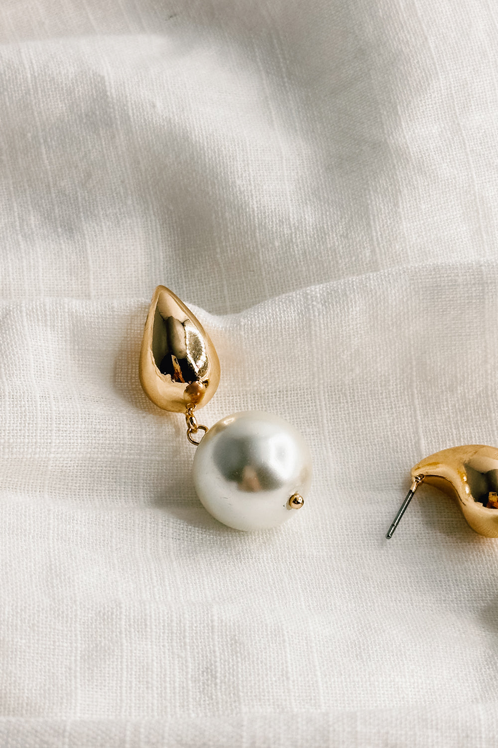 Close up view of the Julie Gold and Pearl Dangle Earring which features gold teardrop shape medallion linked with a pearl medallion